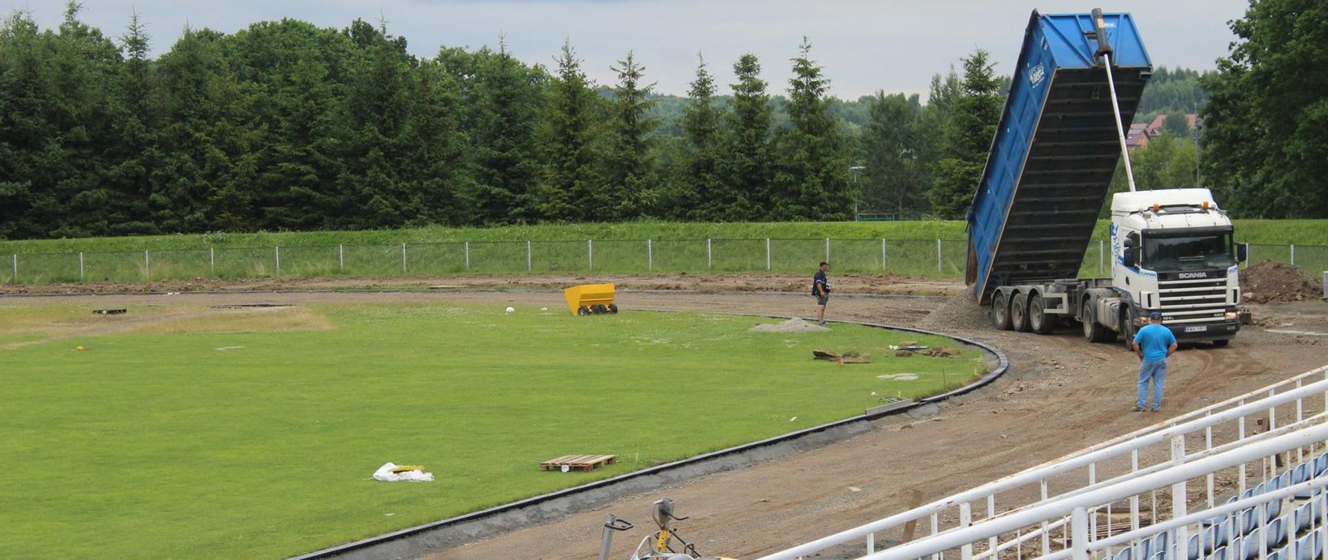 Stadion MKS "Kalwarianka". Na zdjęciu widoczne są prace związane z przebudową bieżni. W głębi po prawej samochód ciężarowy dostarczający piasek na teren obiektu. Po lewej stronie murawa boiska, a na pierwszym planie fragment widowni.