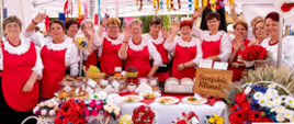 Zdjęcie przedstawiający panie z Kół Gospodyń Wiejskich stojące pod namiotem przy zastawionym stole przekąskami regionalnymi biorący udział w festiwalu „Polska od Kuchni”