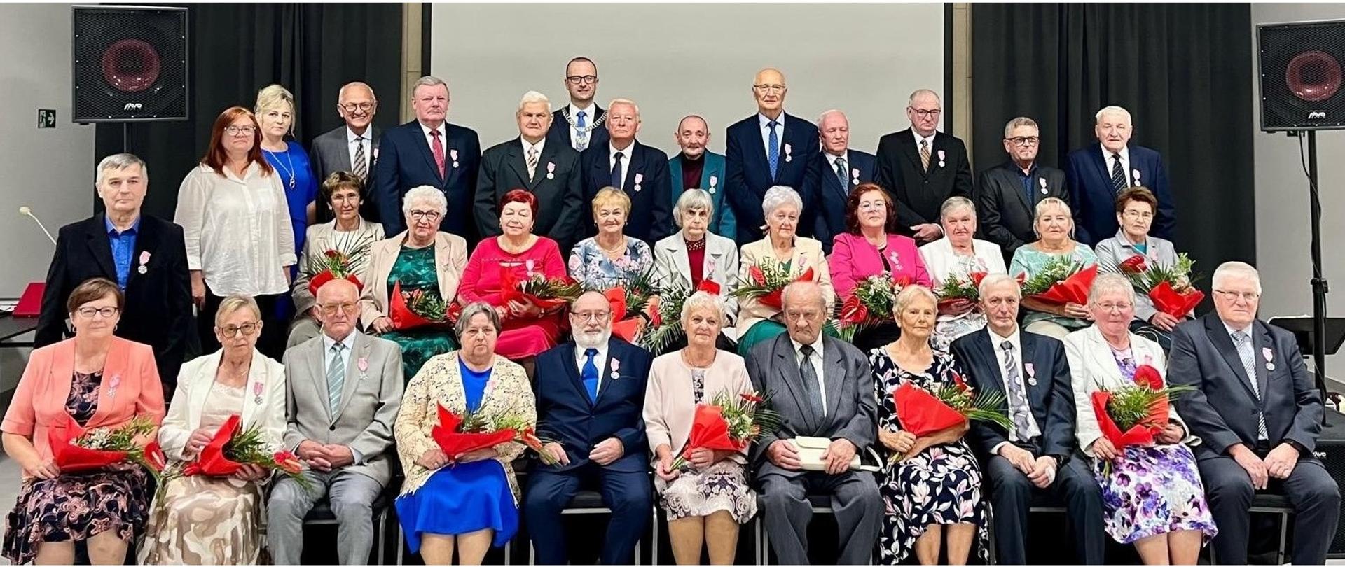 Wspólna fotografia uczestników spotkania. Zebrani siedzą na krzesłach w dwóch rzędach oraz stoją z tyłu
