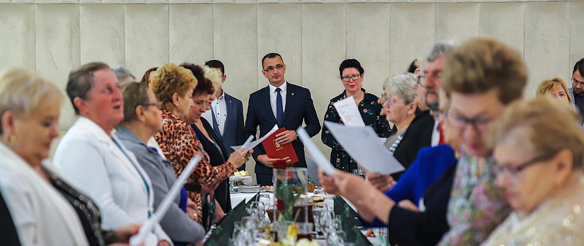 Na zdjęciu uczestnicy spotkania zgromadzeni przy stołach bankietowych.