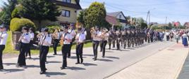 Przemarsz z kościoła na miejsce wydarzenia, orkiestra dęta a za nią żołnierze uczestniczący w odsłonięciu tablicy.