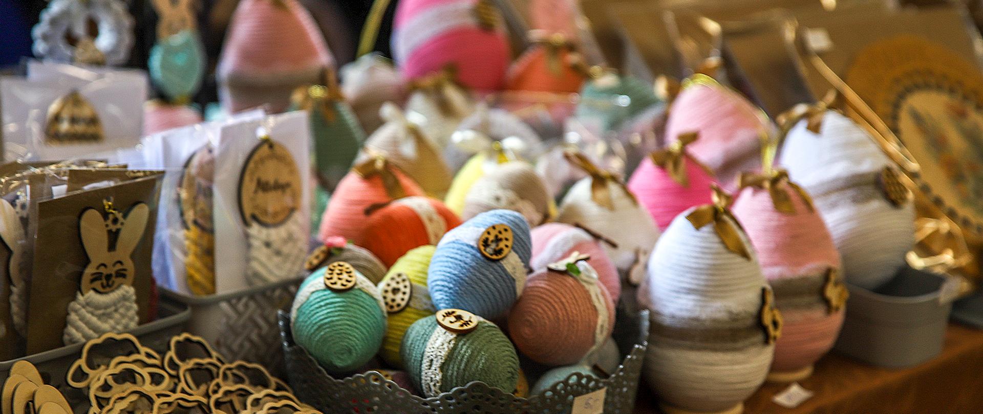 Ręcznie wykonane ozdoby wielkanocne – kolorowe jajka ze sznurka i makramowe zawieszki na stoisku kiermaszowym.