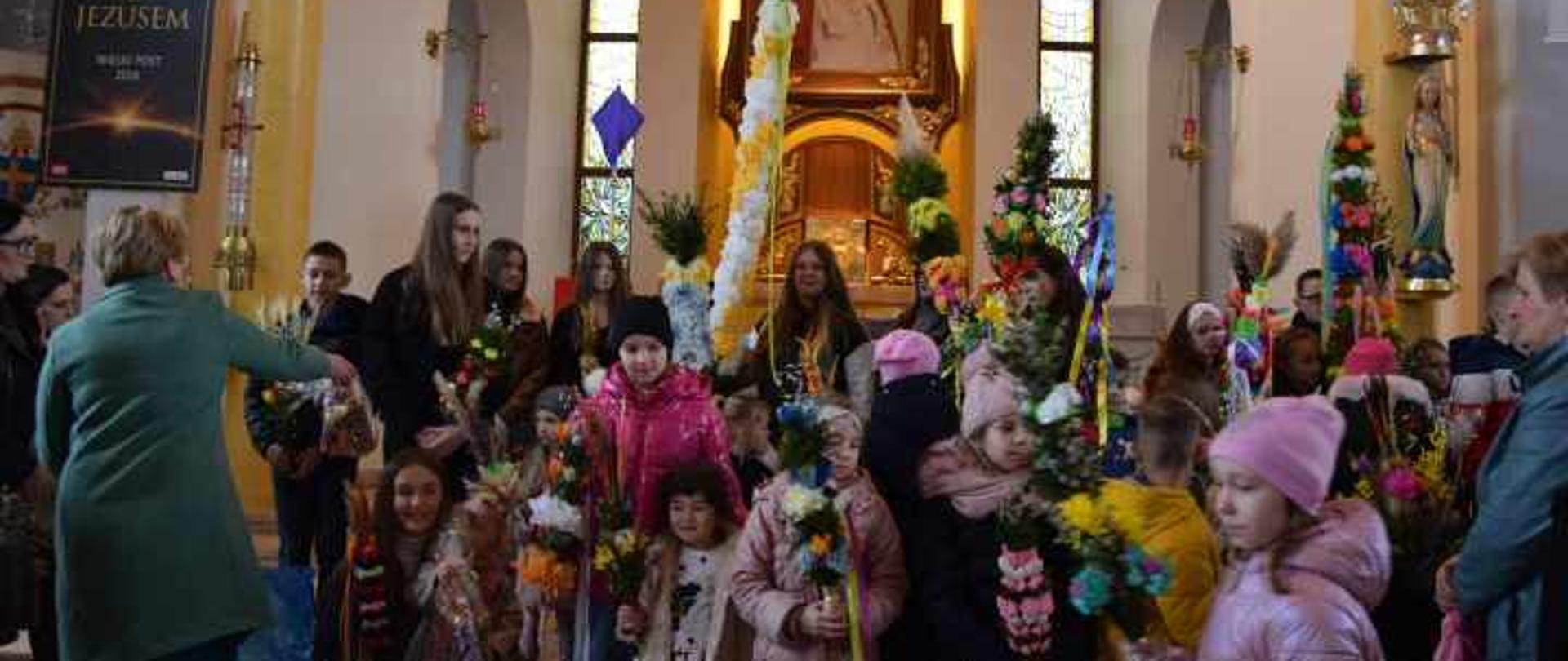 Zdjęcie przedstawia uczestników konkursu pozujących do zdjęć z palmami na tle ołtarza w kościele parafialnym w Podsarniu