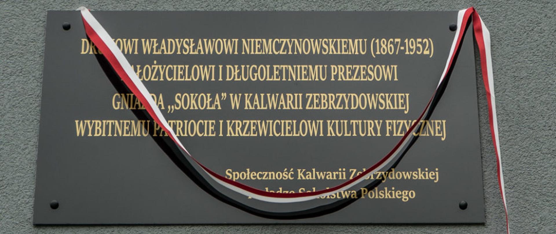 Na zdjęciu okolicznościowa czarna tablica, przepasana biało-czerwono wstęgą. Na tablicy napis: Druhowi Władysławowi Nieczynowskiemu (1867-1952) założycielowi i długoletniemu prezesowi gniazda "Sokoła" w Kalwarii Zebrzydowskiej wybitnemu patriocie i krzewicielowi kultury fizycznej. Społeczność Kalwarii Zebrzydowskiej i władze Sokolstwa Polskiego