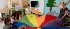 Zabawy w grupie 3latków - dzieci w sali trzymają kolorową płachtę w kształcie koła