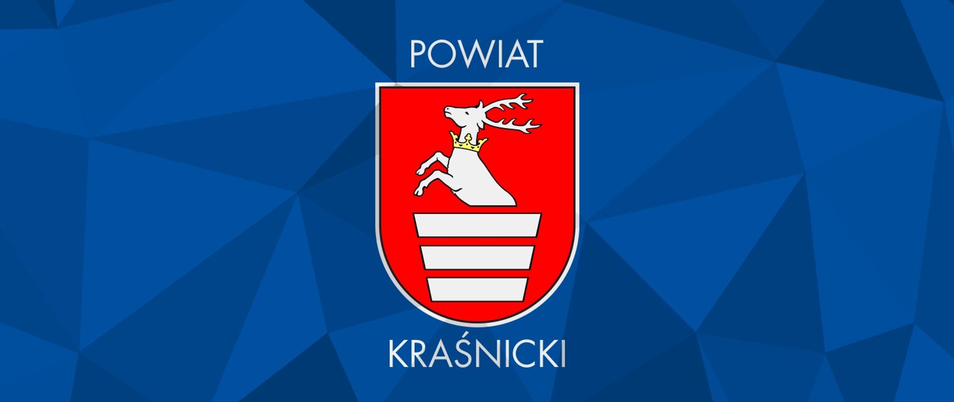 Grafika przedstawia niebieskie tło, na którym znajduje się Herb Powiatu Kraśnickiego wraz z podpisem. Herb na czerwonym tle przedstawia połowę srebrnego jelenia ze złotą koroną na szyi, pod nim znajdują się trzy zwężające się w dół srebrne wręby (białe pasy).