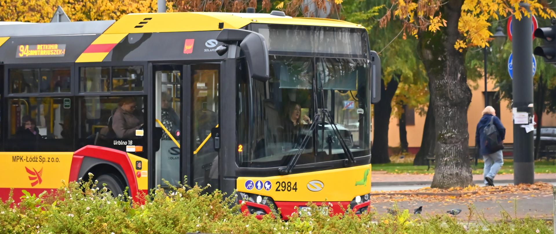Autobus komunikacji miejskiej MPK Łódź na ulicy w jesiennej scenerii, wśród drzew z żółtymi liśćmi.