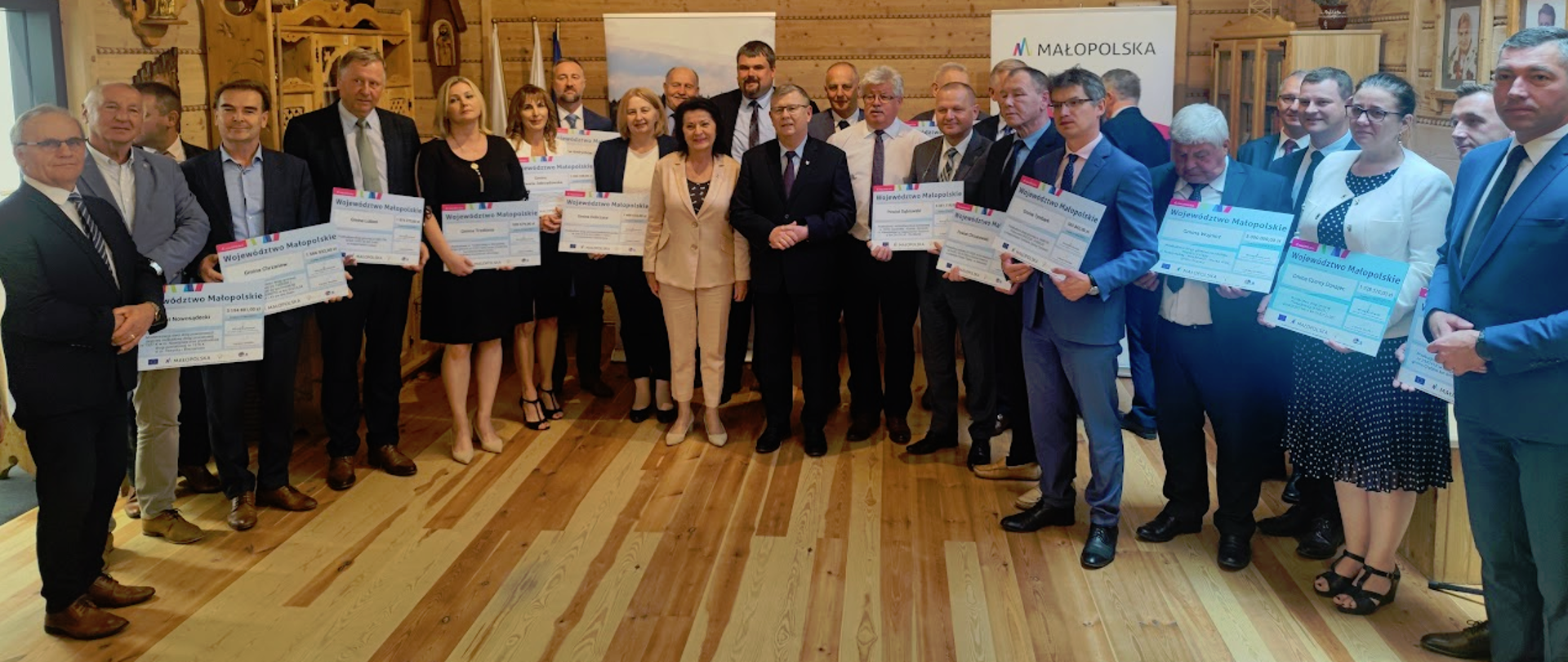 Stoi grupa osób mężczyzn i kobiet, trzymają w ręce czeki 