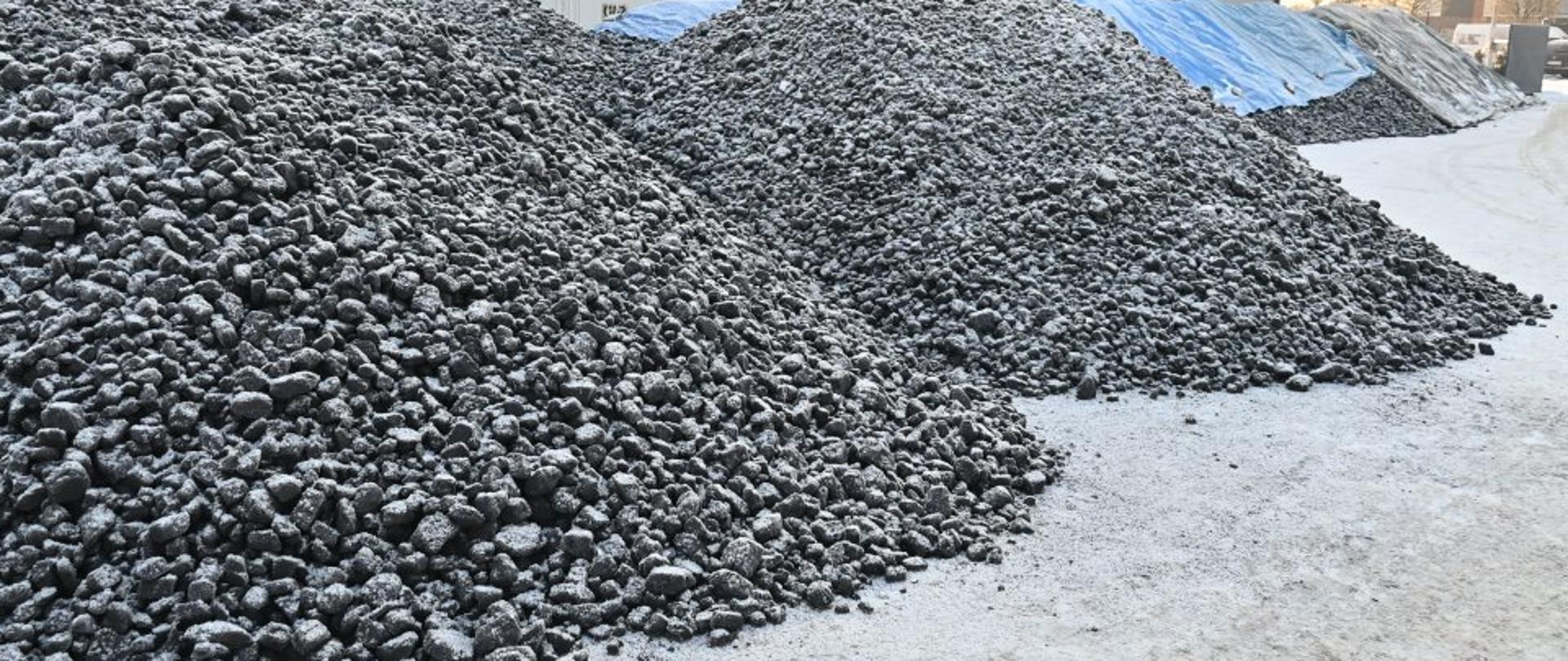 Na pierwszym planie widać węgiel pokryty śniegiem, w tle domy, budynki, drzewa.