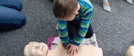 Kurs pierwszej pomocy - chłopiec klęczy przy fantomie, obok siedzą inne dzieci z grupy