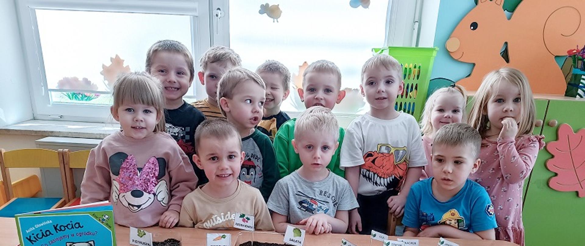 Dzieci pozują do zdjęcia przed przygotowanymi sadzonkami