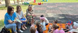 Akcja "Czytanie na polanie" - dzieci siedzą na placu przy budynku przedszkola, rozmawiają z Panią Dyrektor i przedstawicielkami biblioteki