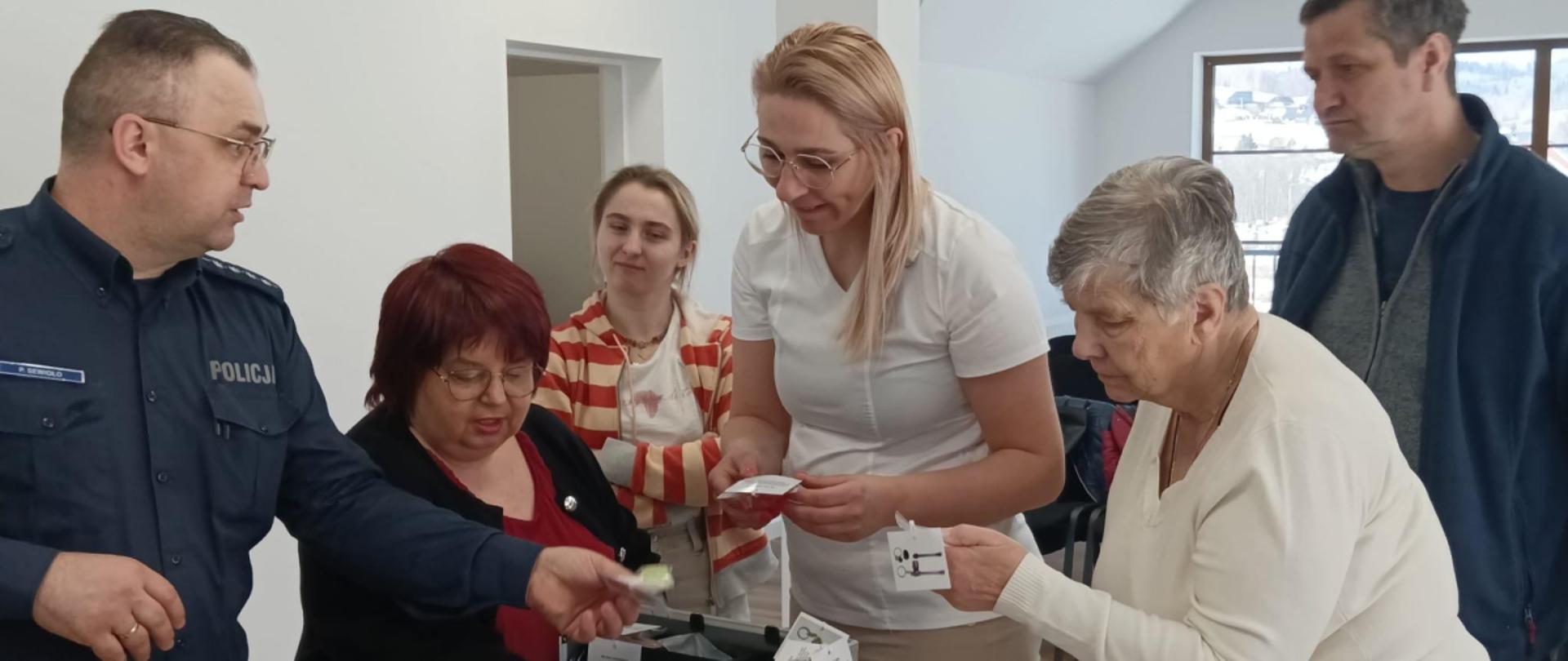 Prezentacja torby z atrapami narkotyków, policjant opowiada uczestnikom spotkania o niebezpieczeństwie związanym z narkotykami w naszym regionie. 