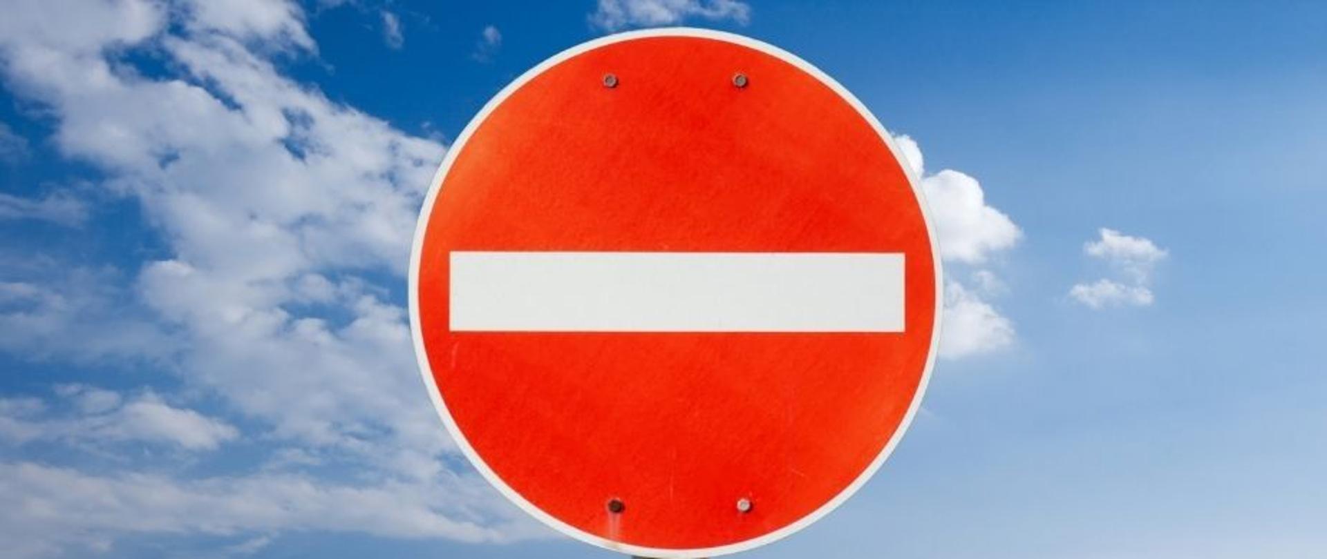 Znak B-2 „zakaz wjazdu" na tle nieba i napis: "parking przy boisku Kalwarianki zamknięty"