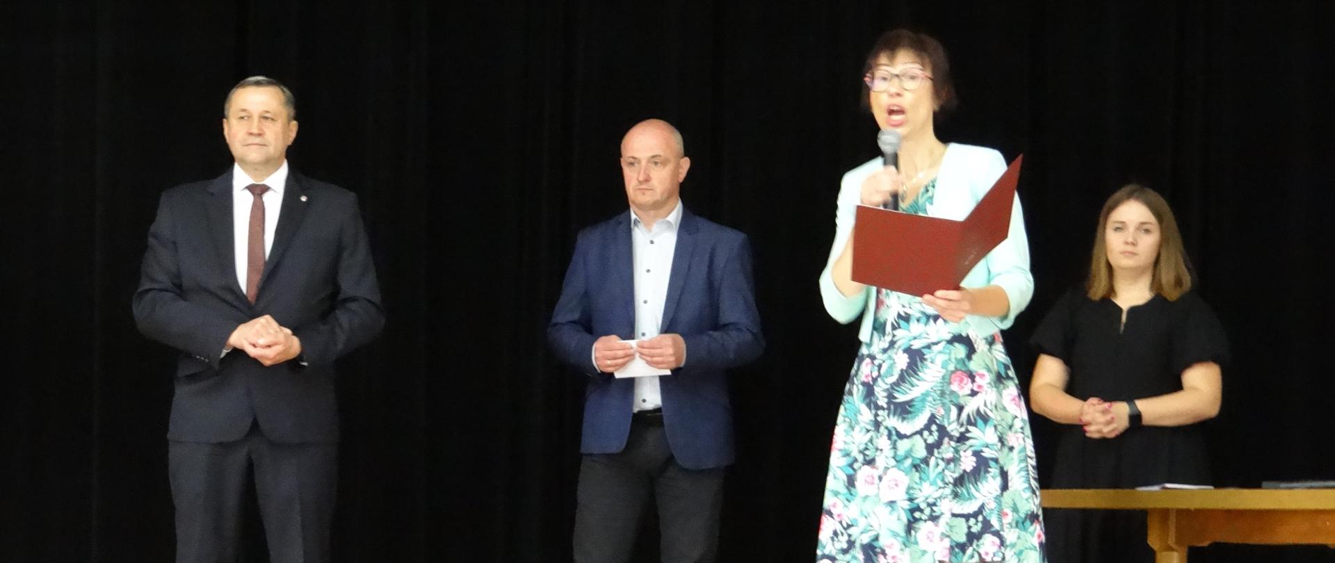 Zdjęcie przedstawia Wójta Gminy pana Tomasza Rajce, przewodniczącego Rady Gminy pana Grzegorza Żądło, Kierownika ZEAS panią Ewę Miśkowiec oraz panią Pauline Świder, stojących na scenie podczas odczytywania dyplomu dla Stypendystów 