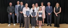 Uczniowie ze szkoły w Harkabuzie wspólnie z p. dyrektorem, panem wójtem, zastępcą wójta, panią Ewą Miśkowiec oraz pracownikiem ZEAS. Wszyscy pozują do zdjęcia na scenie w remizie OSP.