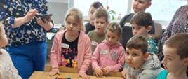 Dzieci stoją przy stole, na którym leżą materiały edukacyjne - karciana gra
