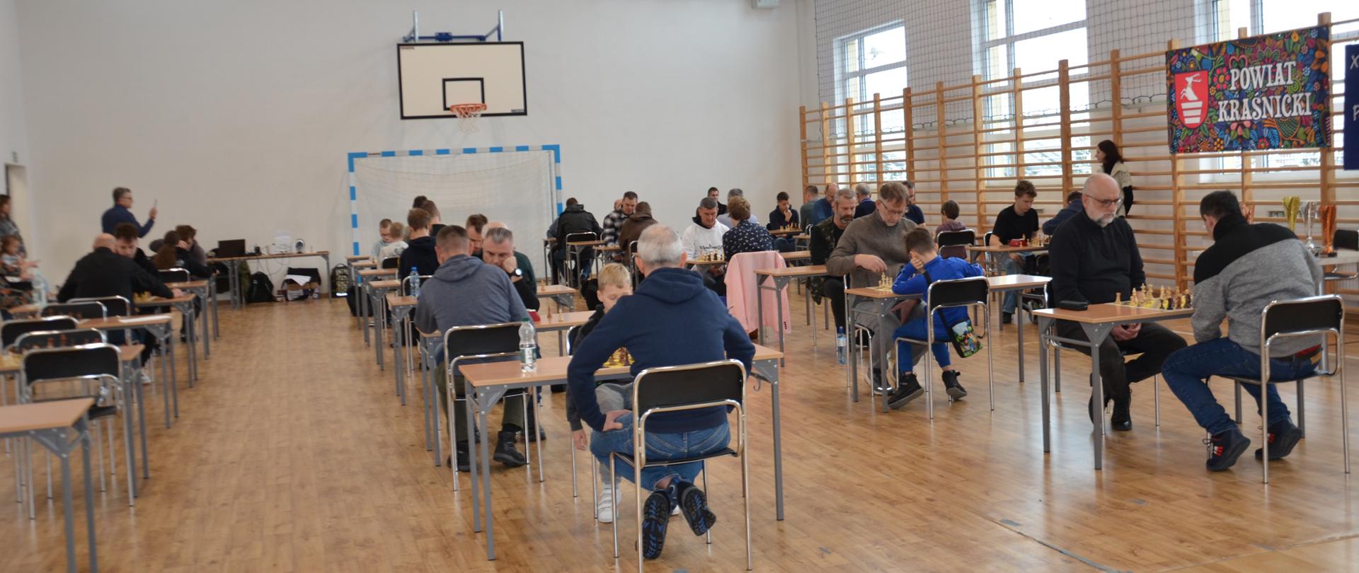 Zawodnicy turnieju podczas rozgrywania partii szachowych na sali gimnastycznej.