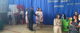Mężczyzna w garniturze stoi na przeciwko dwóch kobiet i podaje prawą rękę kobiecie po prawej