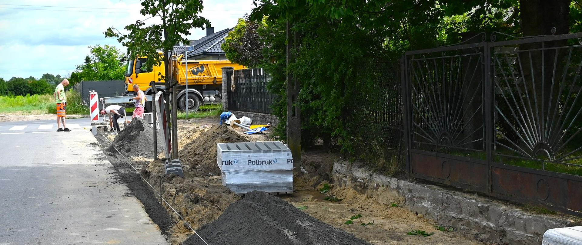 Rozkopany chodnik, w tle samochód budowlany. 