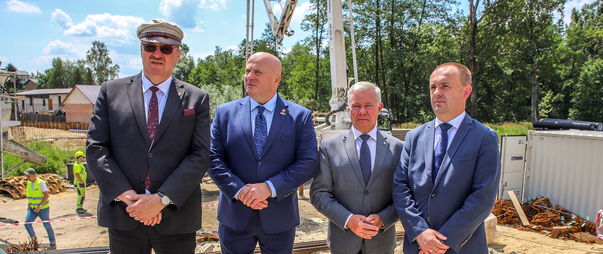 Na zdjęciu uczestnicy spotkania z dziennikarzami pozują do zdjęcia na tle prac budowlanych.`