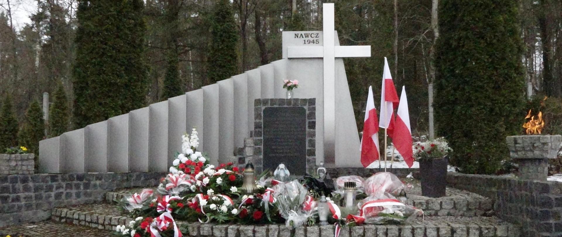 Zdjęcie pomnika ofiar Marszu Śmierci KL Stutthof ze złożonymi kwiatami na tle lasu