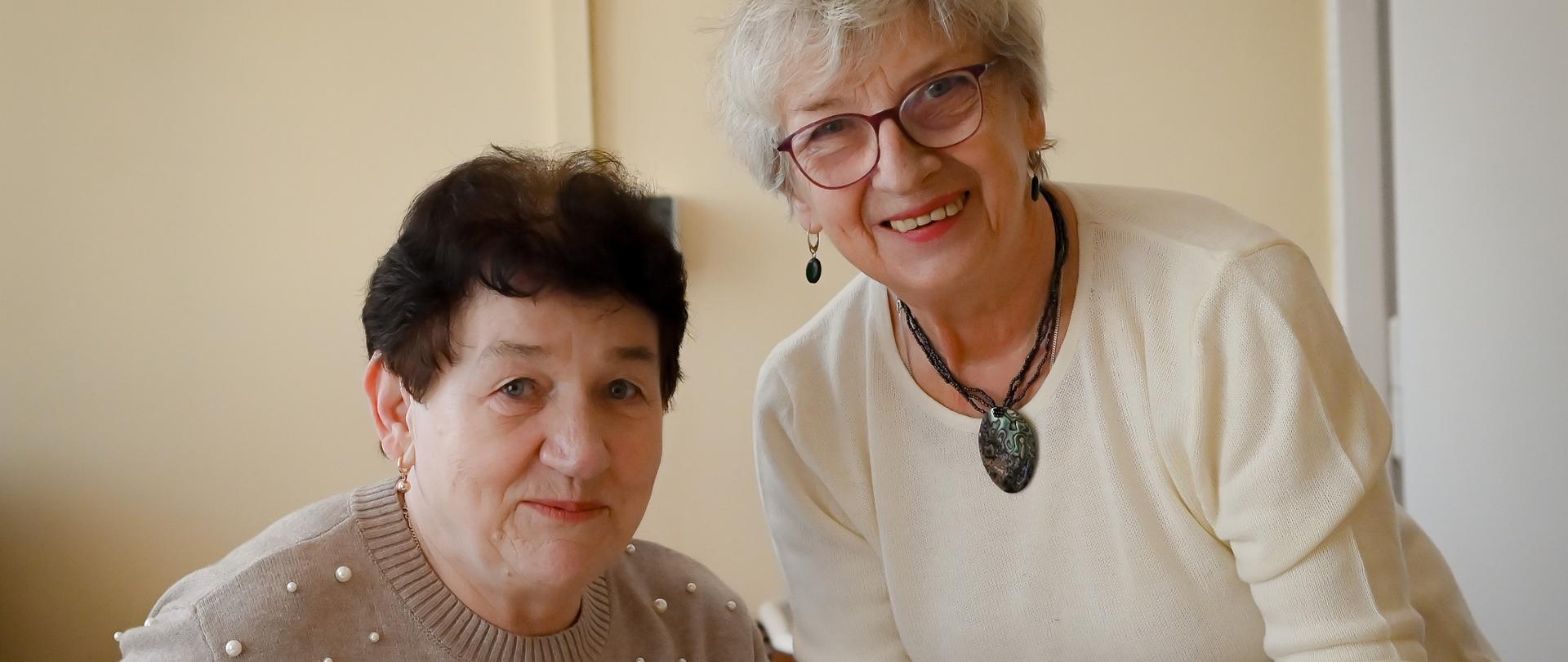 Dwie seniorki przygotowują posiłek przy stole w jasnym wnętrzu.