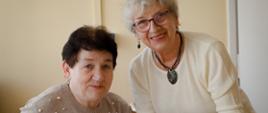 Dwie seniorki przygotowują posiłek przy stole w jasnym wnętrzu.