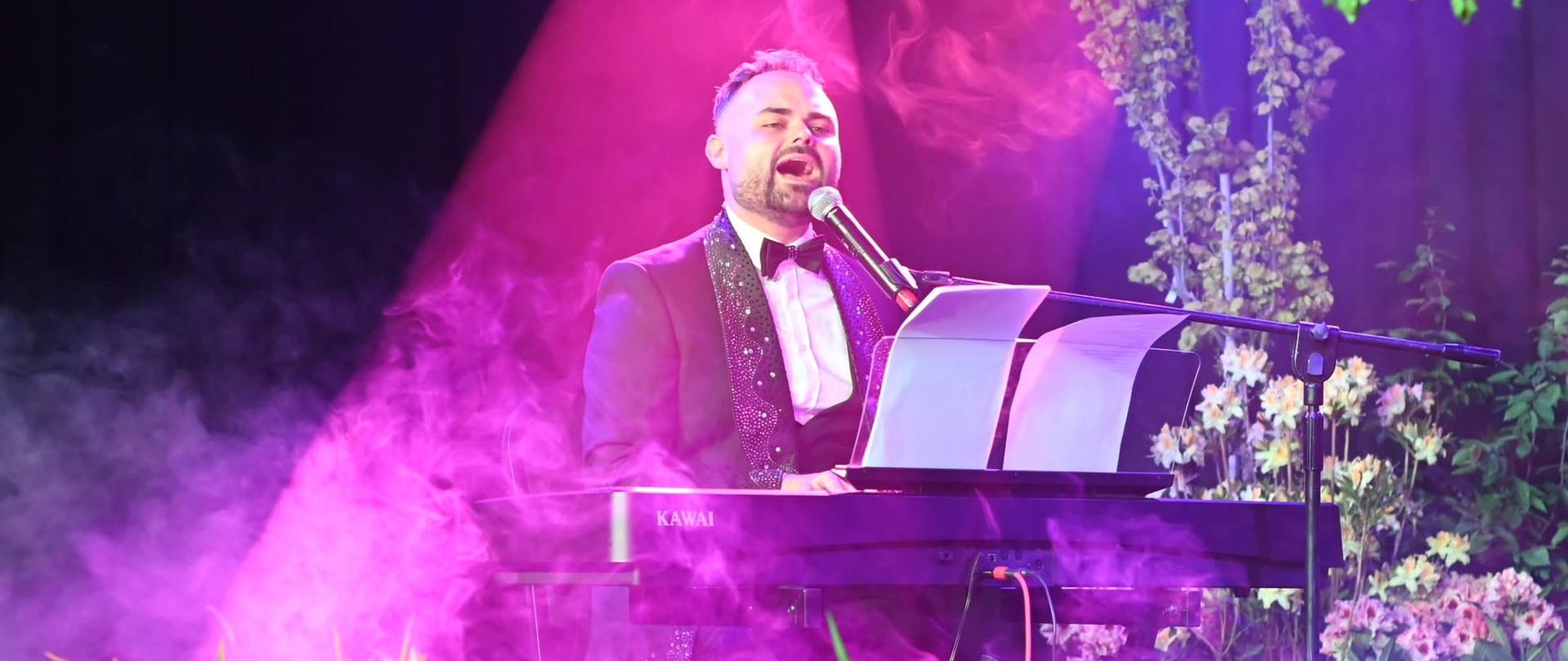 Pianista i wokalista występuje na scenie wśród kwiatów i efektów świetlnych podczas koncertu festiwalowego.