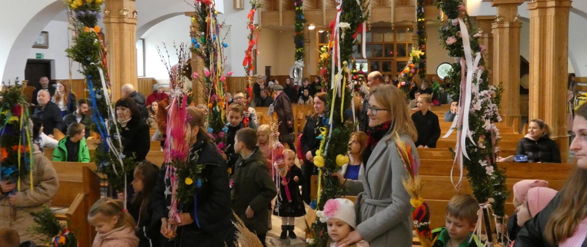 Zdjęcie przedstawia stojących w kościele wiernych trzymających palmy wielkanocne