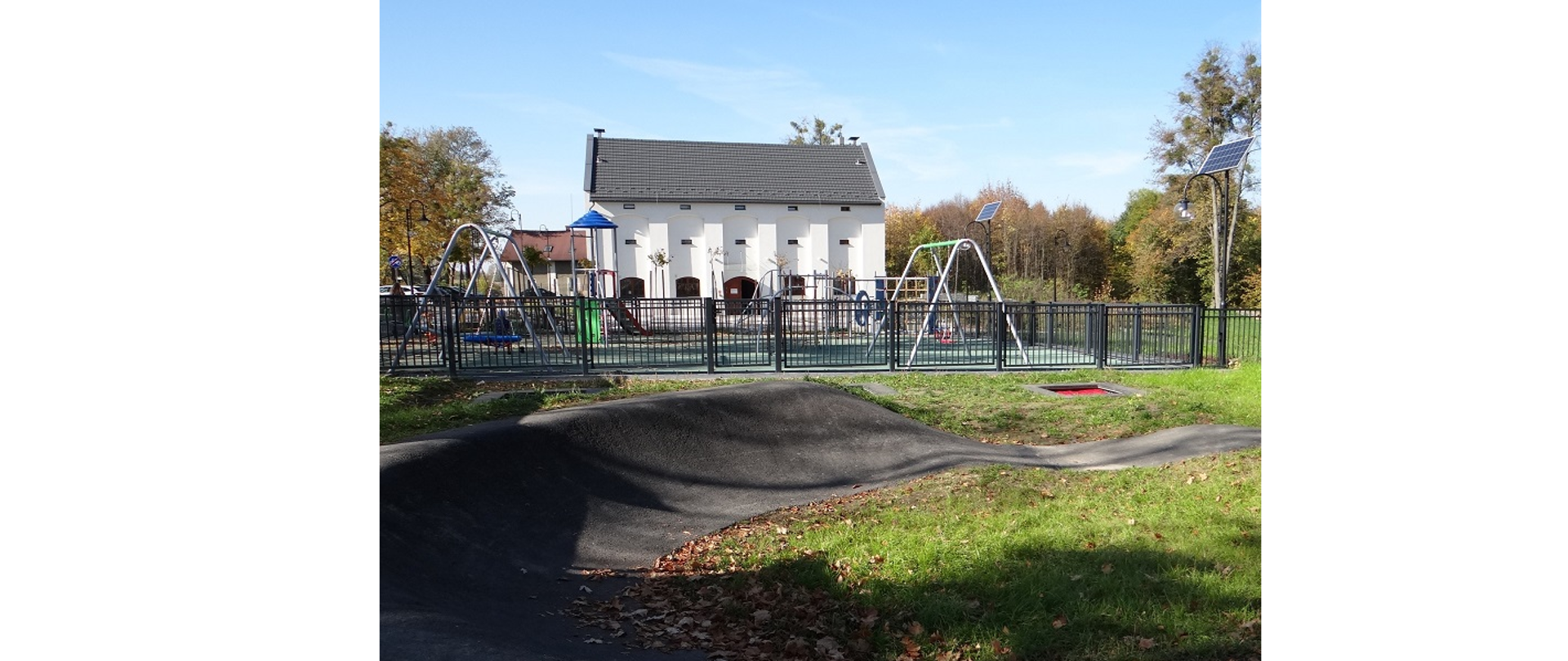 Pumptrack dla dzieci i plac zabaw przed Domem Przyrodnika. Na pierwszym planie pumptrack dla dzieci, na drugimi plac zabaw, na trzecim Dom Przyrodnika