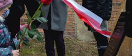 Tablica czarna ze złotym napisem umieszczona na kamieniu a przed nią dziecko z różą