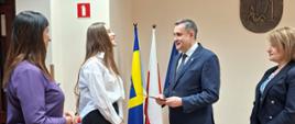 Wójt Gminy Raba Wyżna pan Tomasz Rajca wręcza Wręcza wyróżnienie Gabrieli Urbaniak. W tle flaga Gminy oraz flaga Polski. Z lewej strony Pani Dorota Urbaniak,z prawej Skarbnik Gminy Raba Wyżna pani Beata Kalemba.