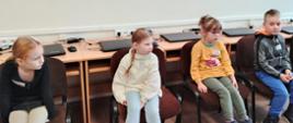 Dzieci siedzą na krzesłach w sali informatycznej