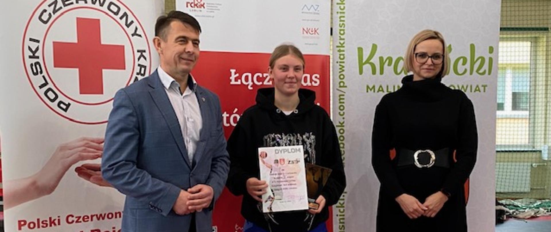 Wręczenie nagrody zawodniczce (w środku). Od lewej stoi Przewodniczący Rady Powiatu w Kraśniku pan Jacek Dubiel, zaś po prawej stronie Wicedyrektor Zespołu Szkół nr 3 w Kraśniku pani Monika Gozdalska