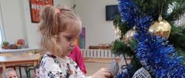 Dziewczynka stoi przy choince, dekoruje ją