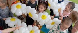 Zajęcia w przedszkolu - dzieci stoją z balonami w kształcie kwiatów 
