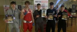 Pięciu zawodników Klubu Bokserskiego "Sparta" Kraśnik stoi w szeregu w hali sportowej na tle licznych banerów reklamowych. W dłoniach trzymają dyplomy, a na szyjach mają zawieszone medale.