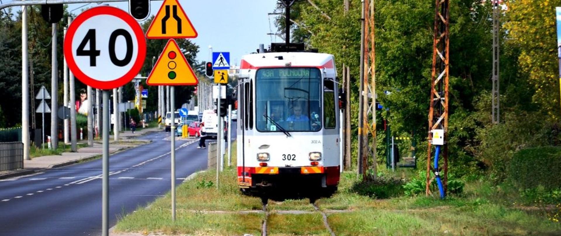 Na zdjęciu w centrum widać stary tramwaj 43A do zajezdni Północna jadący po szynach. Po lewej widzimy ulicę a obok znaki drogowe sygnalizujące przejście dla pieszych wraz z światłami oraz ograniczenie prędkości do 40 kilometrów na godzinę.