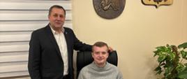 Wójt Gminy Raba Wyżna Tomasz Rajca oraz Paweł Myrda. Paweł siedzi na fotelu przy biurku Wójta. Wójt stoi obok i ręką podpiera się o zagłówek fotela