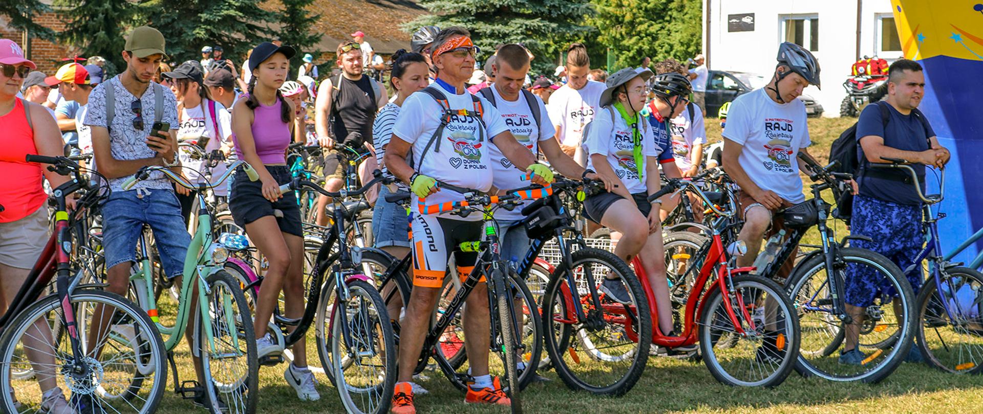 Na zdjęciu grupa uczestników rajdu rowerowego czekających na miejscu startu. Uczestnicy mają na sobie pamiątkowe koszulki z nazwą radju.