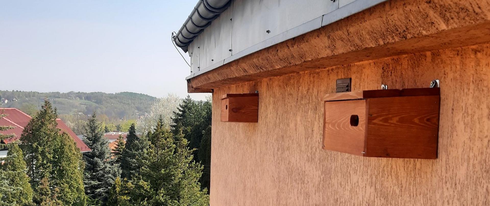 Na pierwszym planie budka lęgowa dla jerzyków, zawieszona na budynku. W tle widok na Kalwarię Zebrzydowską. 