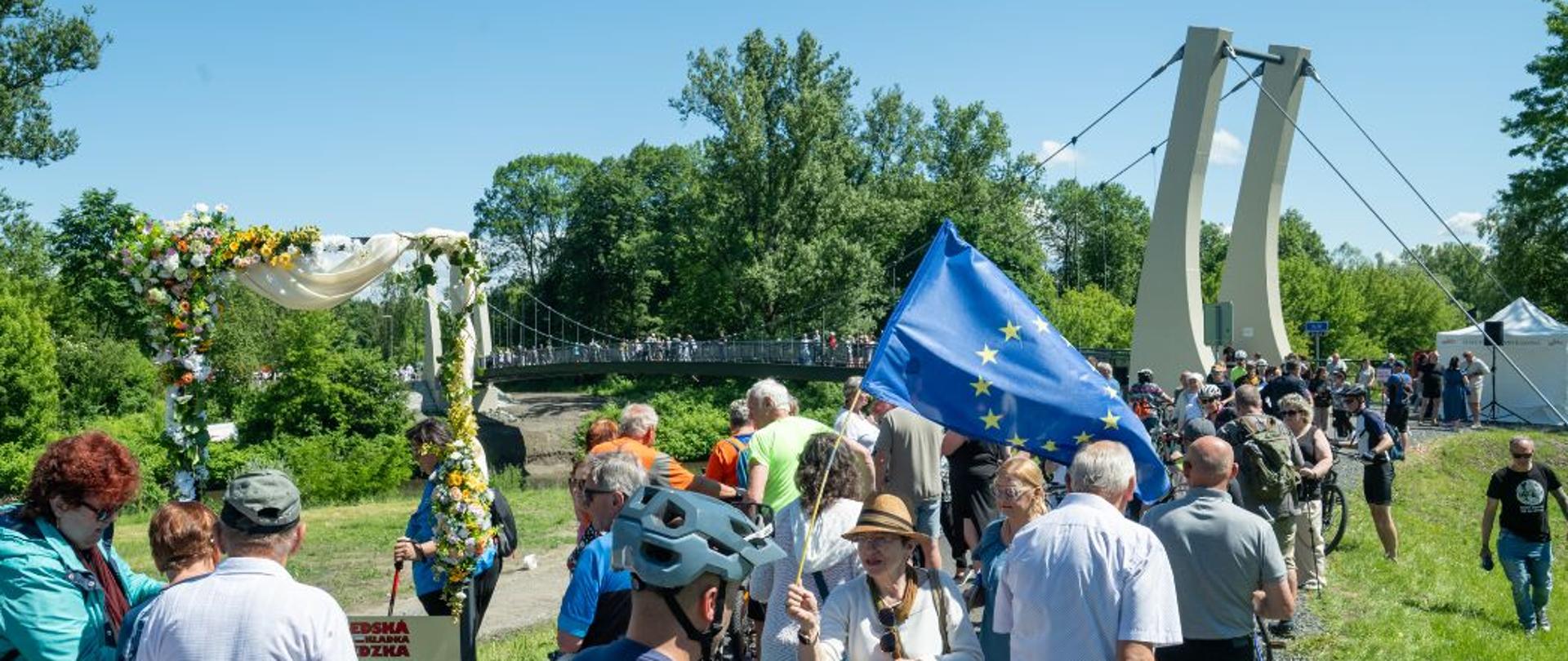Kolejka do kładki od czeskiej strony. Jedna z osób w tłumie trzyma podniesioną flagę UE. Widoczne także rowery. Fot. Sebastian Jurga (Arch. UG Hażlach) 