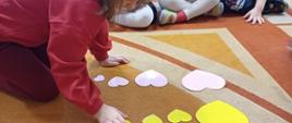 Dzieci siedzą na dywanie, układają papierowe serca