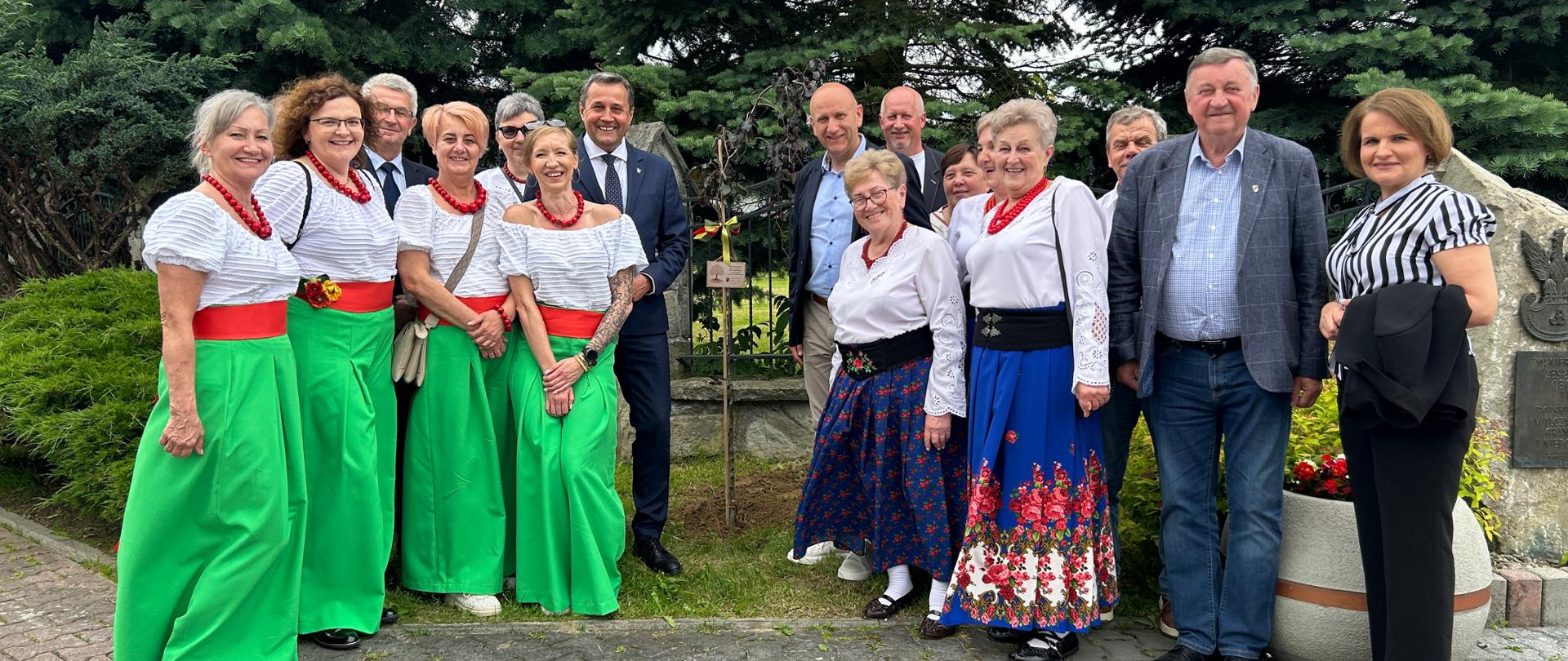 Grupa osób pozuje do zdjęcia na zewnątrz, na tle drzew.