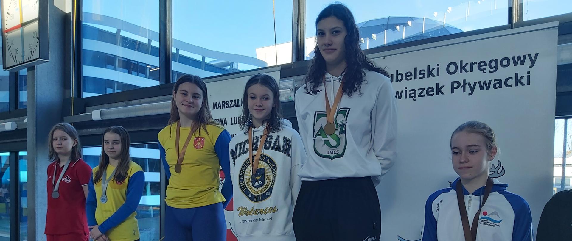 Zdjęcie przedstawia sześć zawodniczek stojących na podium po uroczystym wręczeniu medali. Trzecia od lewej, na pierwszym stopniu podium, stoi zawodniczka Fali Kraśnik Amelia Wysocka