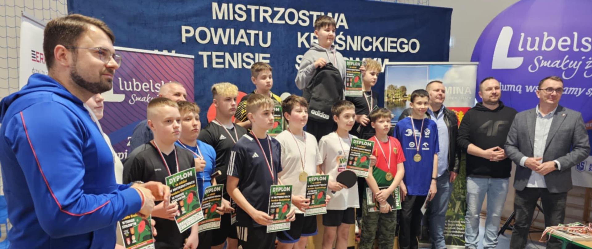 W lekkim półokręgu, pośrodku, na tle baneru z nazwą imprezy oraz rollupów współorganizatorów stoją nagrodzeni chłopcy w jednej z kategorii wiekowych. W rękach trzymają dyplomy, a na ich szyjach wiszą medale. Jako pierwszy od prawej strony stoi Wicestarosta Kraśnicki Paweł Kudrel, zaś obok niego Wójt Gminy Trzydnik Duży Krzysztof Serafin. Z lewej strony stoi Prezes Stowarzyszenia Wschód Lubelskich Serc Michał Stawiarski.