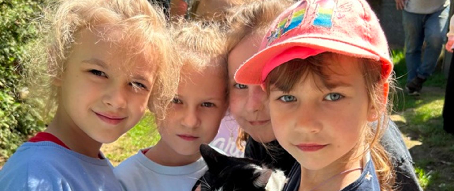 Dzieci pozują do zdjęcia, wspólnie trzymając kota na rękach