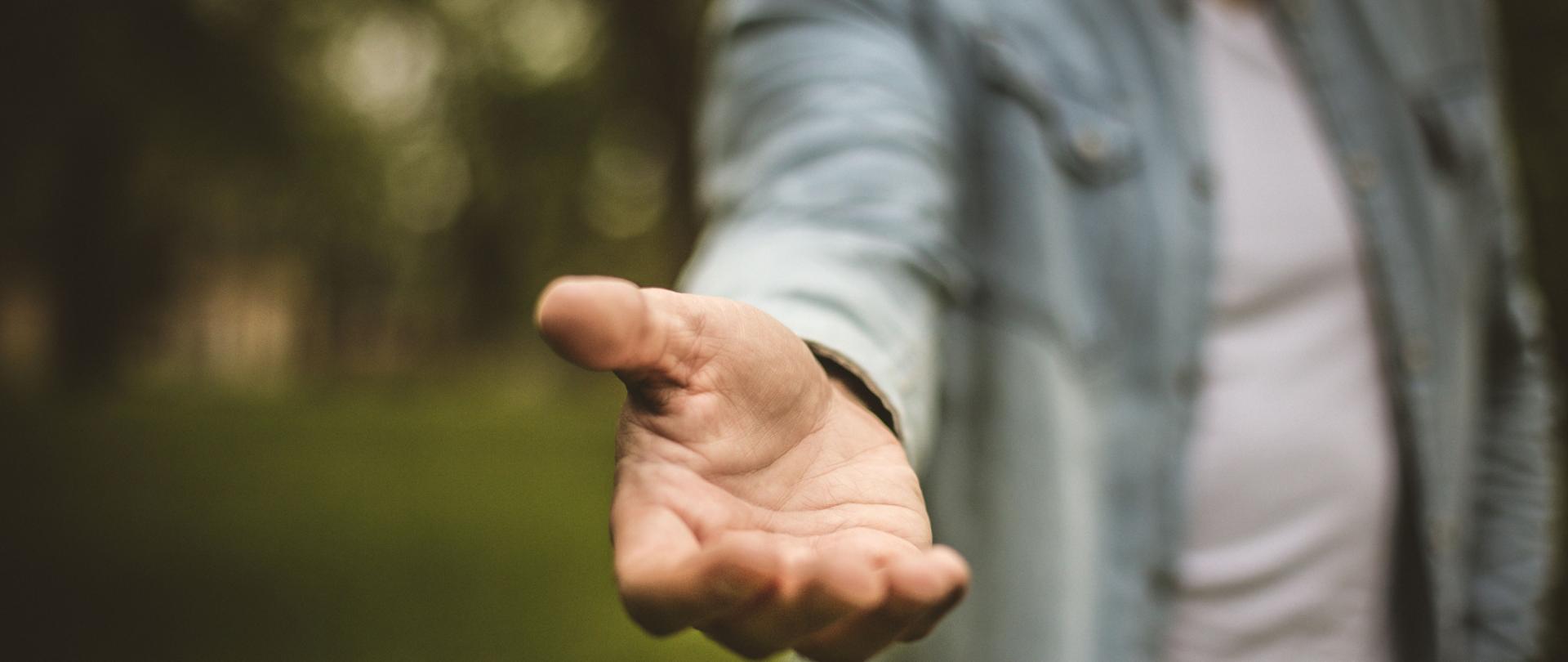 Na zielonym tle wyciągnięta pomocna dłoń 