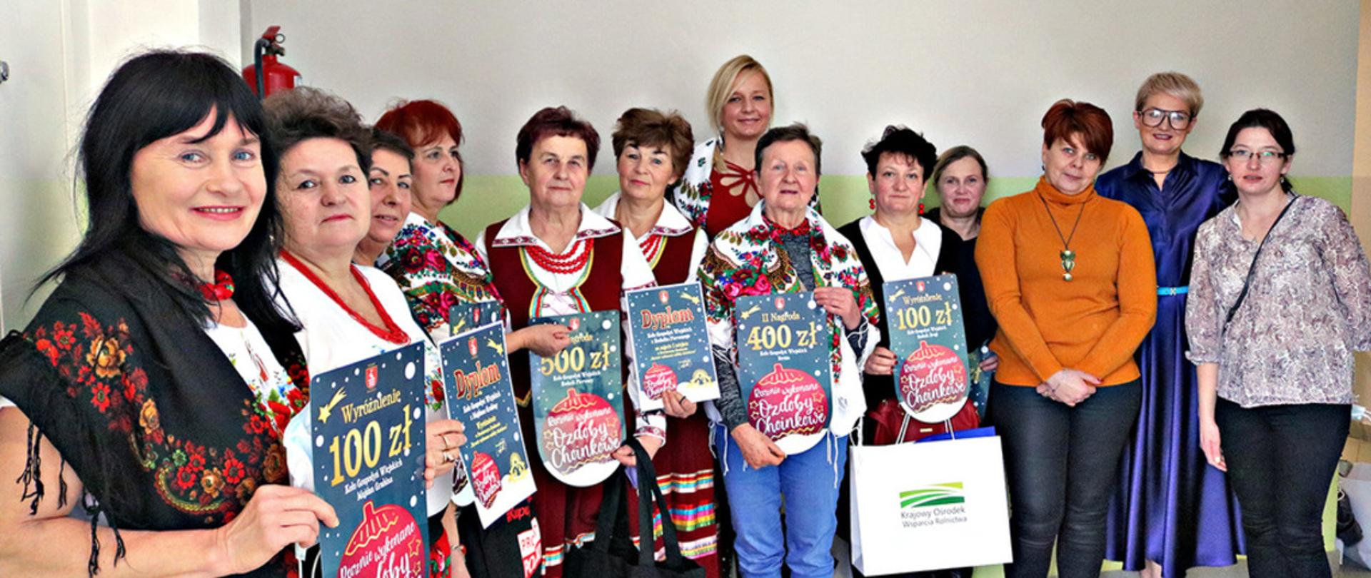 Dwanaście pań z Kół Gospodyń Wiejskich z Powiatu Kraśnickiego stojące z bonami i dyplomami oraz Wicedyrektor Krajowego Ośrodka Wsparcia Rolnictwa Oddział Terenowy w Lublinie Anna Baluch.